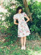 Woman in a floral dress standing in a natural setting with greenery.
