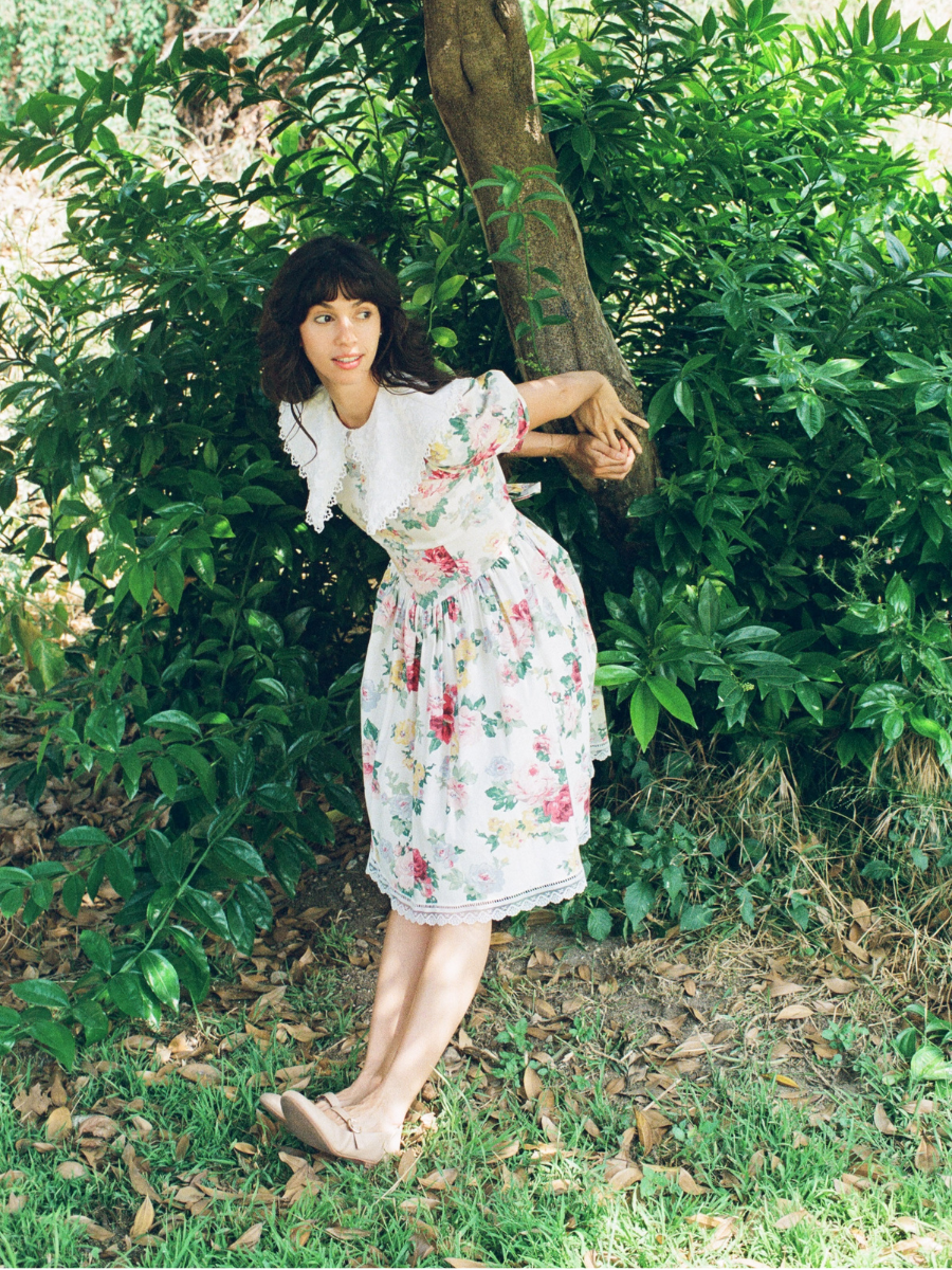 Woman in a floral dress standing in a natural setting with greenery