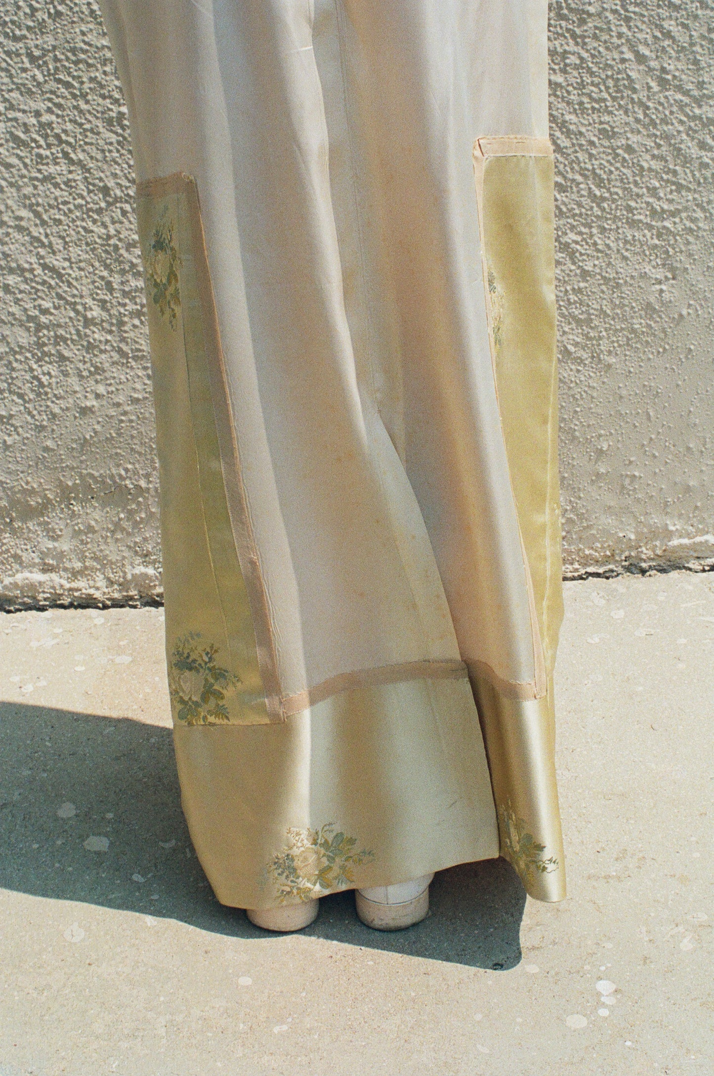 Light-colored fabric with floral patterns draped over a surface against a textured wall.