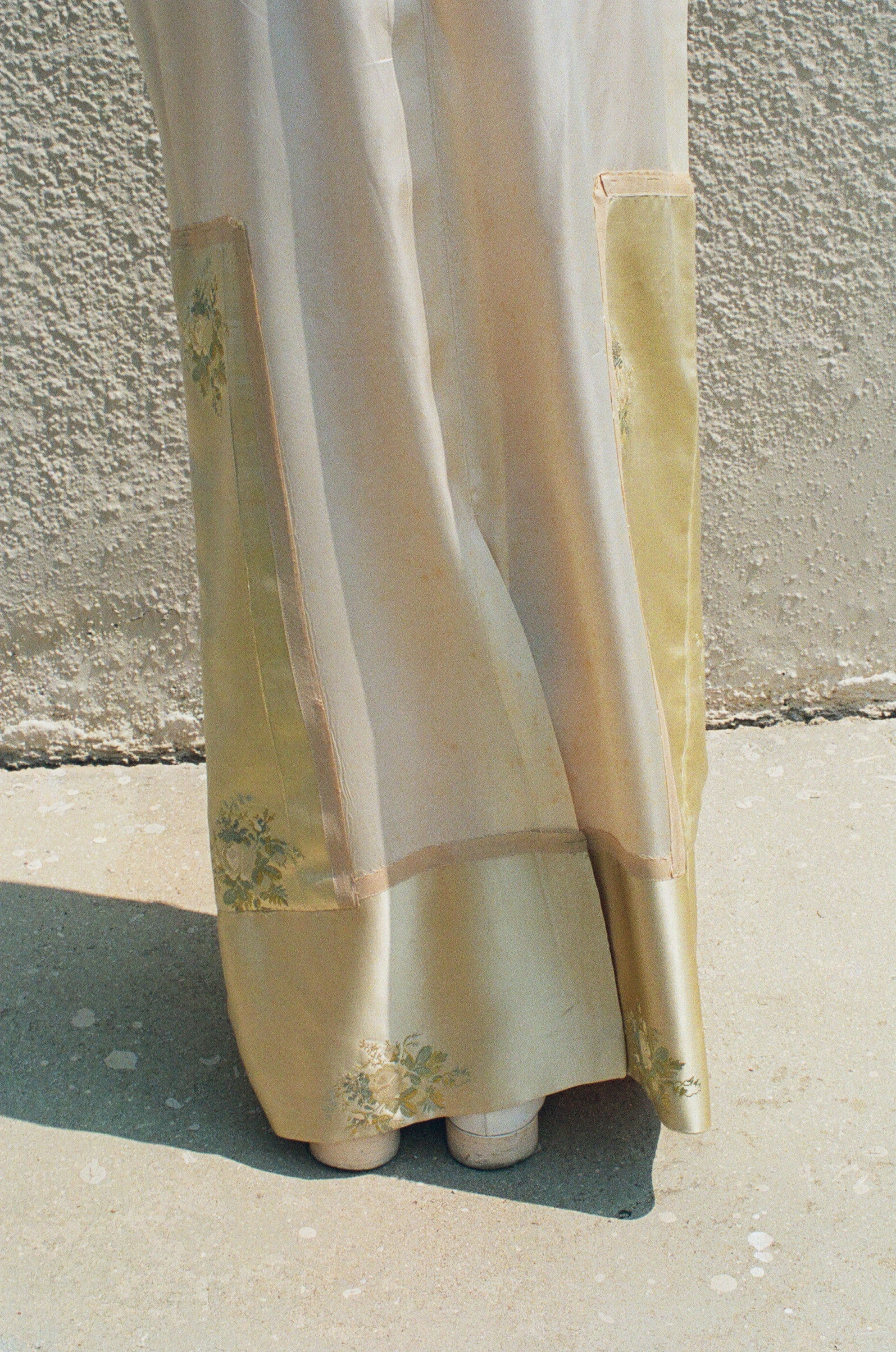 Light-colored fabric with floral patterns draped over a surface against a textured wall.