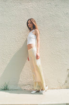 Woman in a white top and beige pants standing against a light-colored wall.