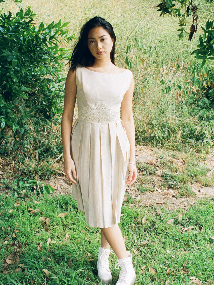 Woman in a white dress standing in a natural setting with greenery.
