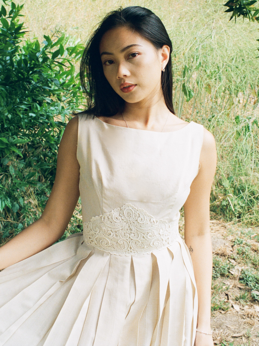 Woman in a white dress with lace detail standing outdoors.