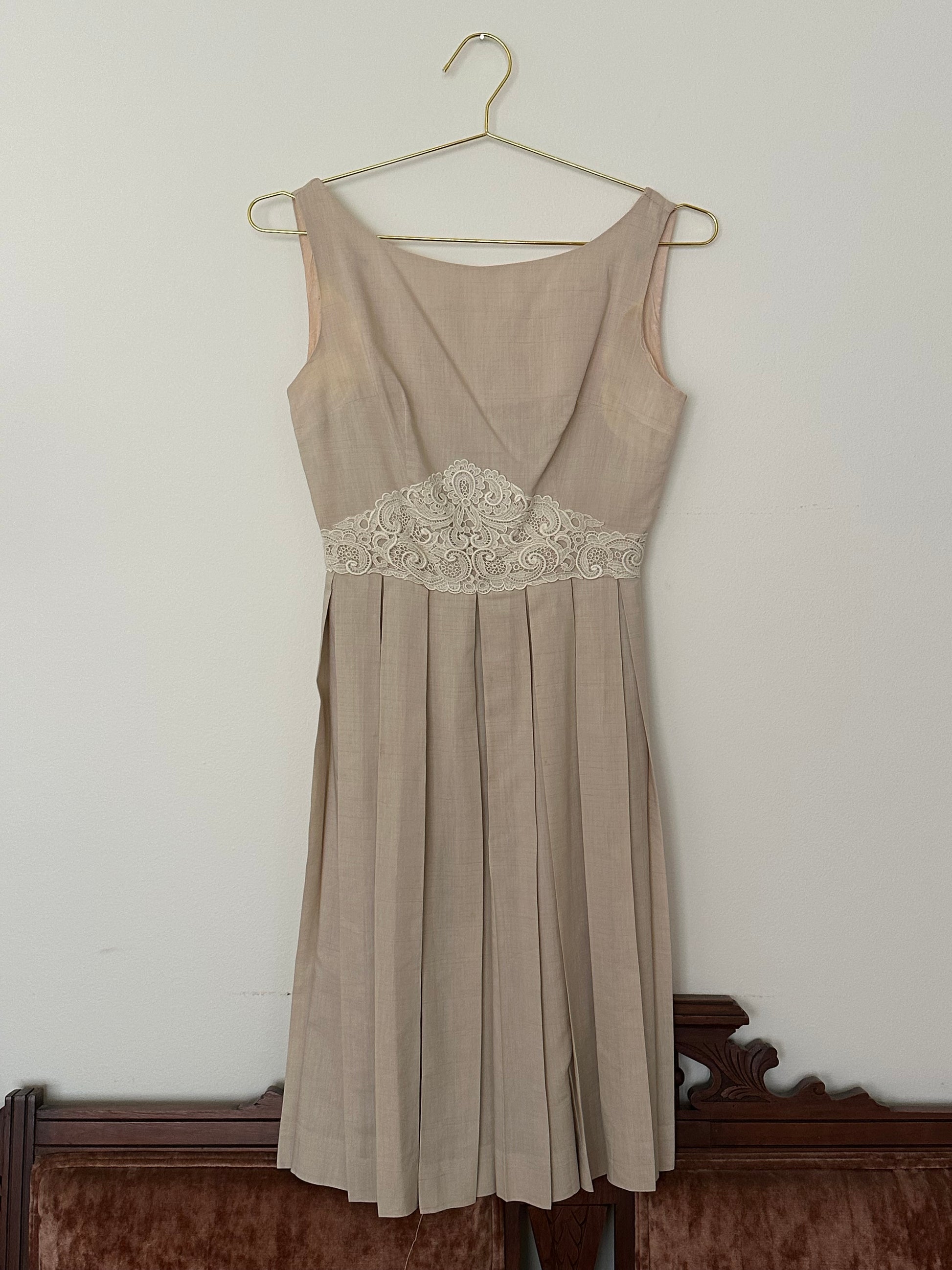Beige dress with lace detail on a hanger against a plain background