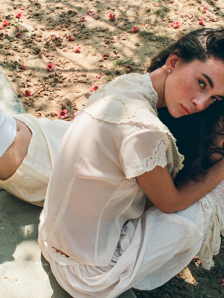 Woman in a white dress sitting on the ground with flowers around