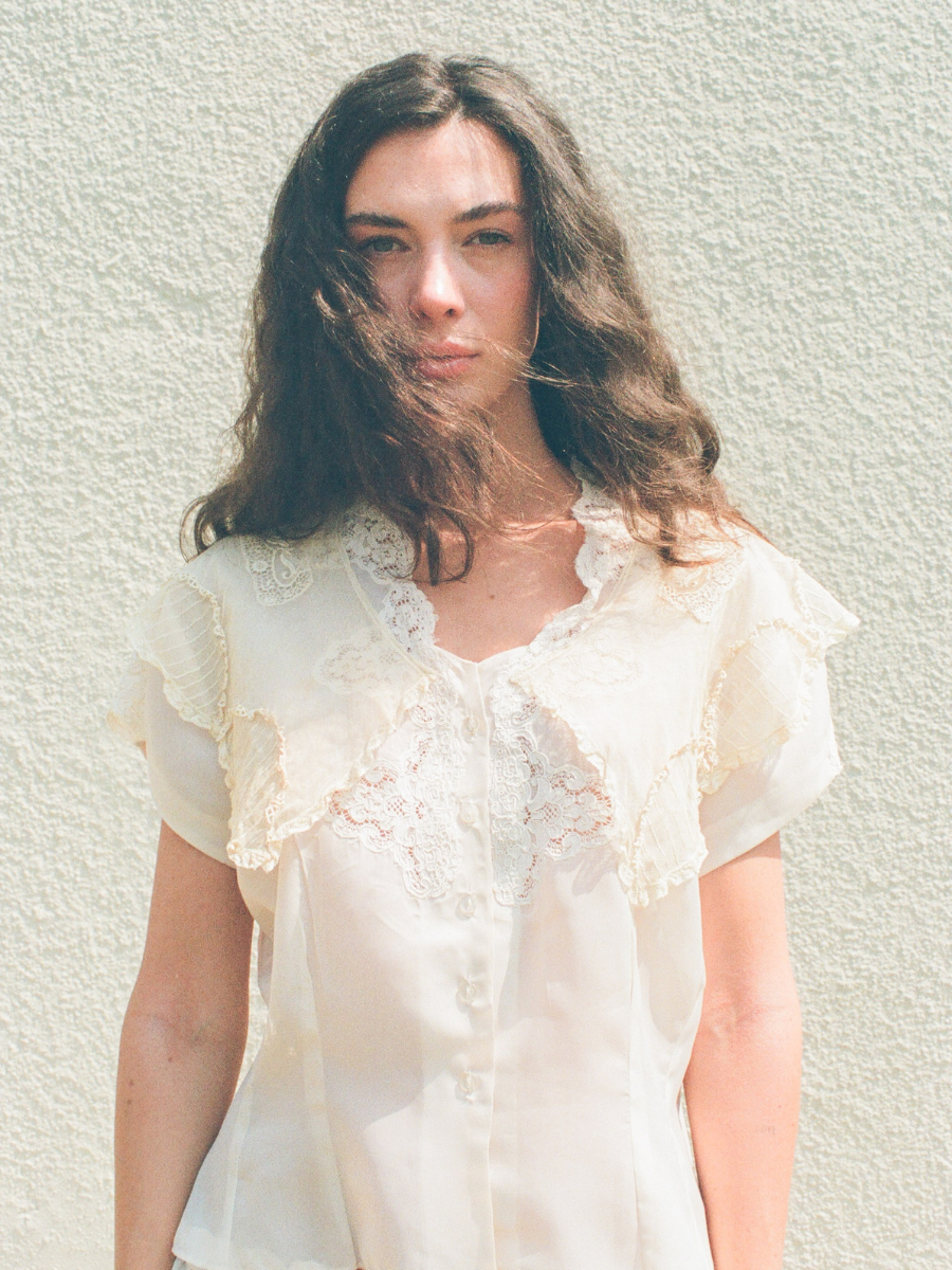 Woman wearing a light-colored blouse against a textured wall