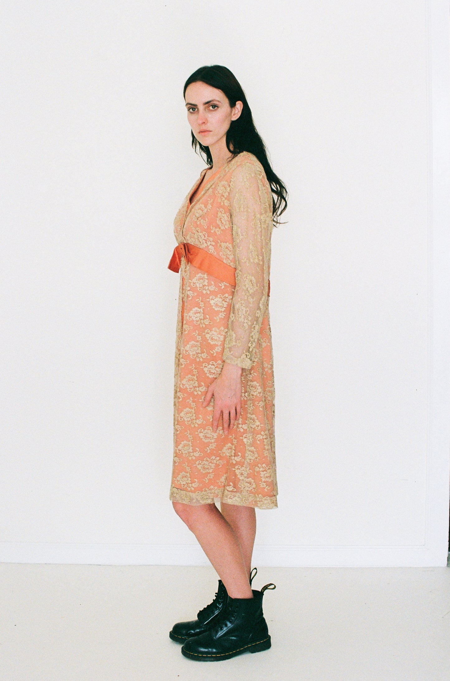 Woman wearing a patterned dress with an orange belt and black boots on a white background