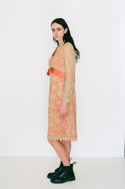 Woman wearing a patterned dress with an orange belt and black boots on a white background