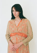 Woman wearing a floral dress with an orange belt against a white background