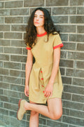 Woman wearing a beige dress with red accents against a brick wall