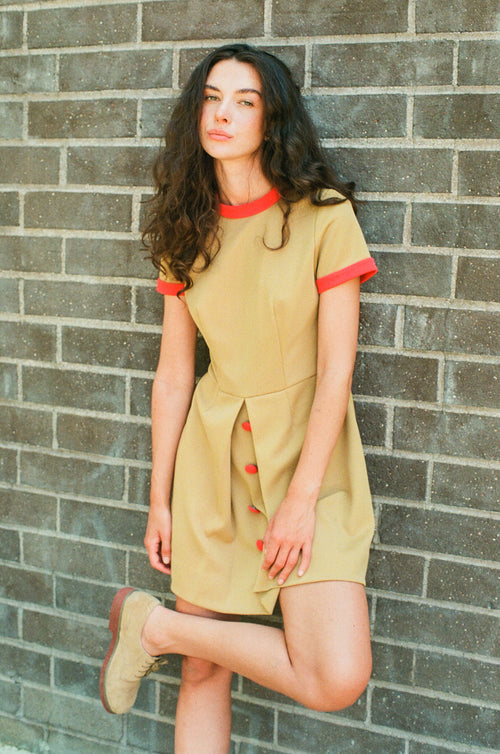 Woman wearing a beige dress with red accents against a brick wall