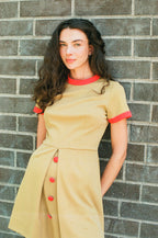 Woman wearing a beige dress with red accents against a brick wall