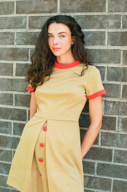 Woman wearing a beige dress with red accents against a brick wall