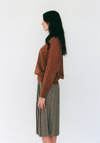 Woman wearing a brown sweater and plaid skirt against a white background