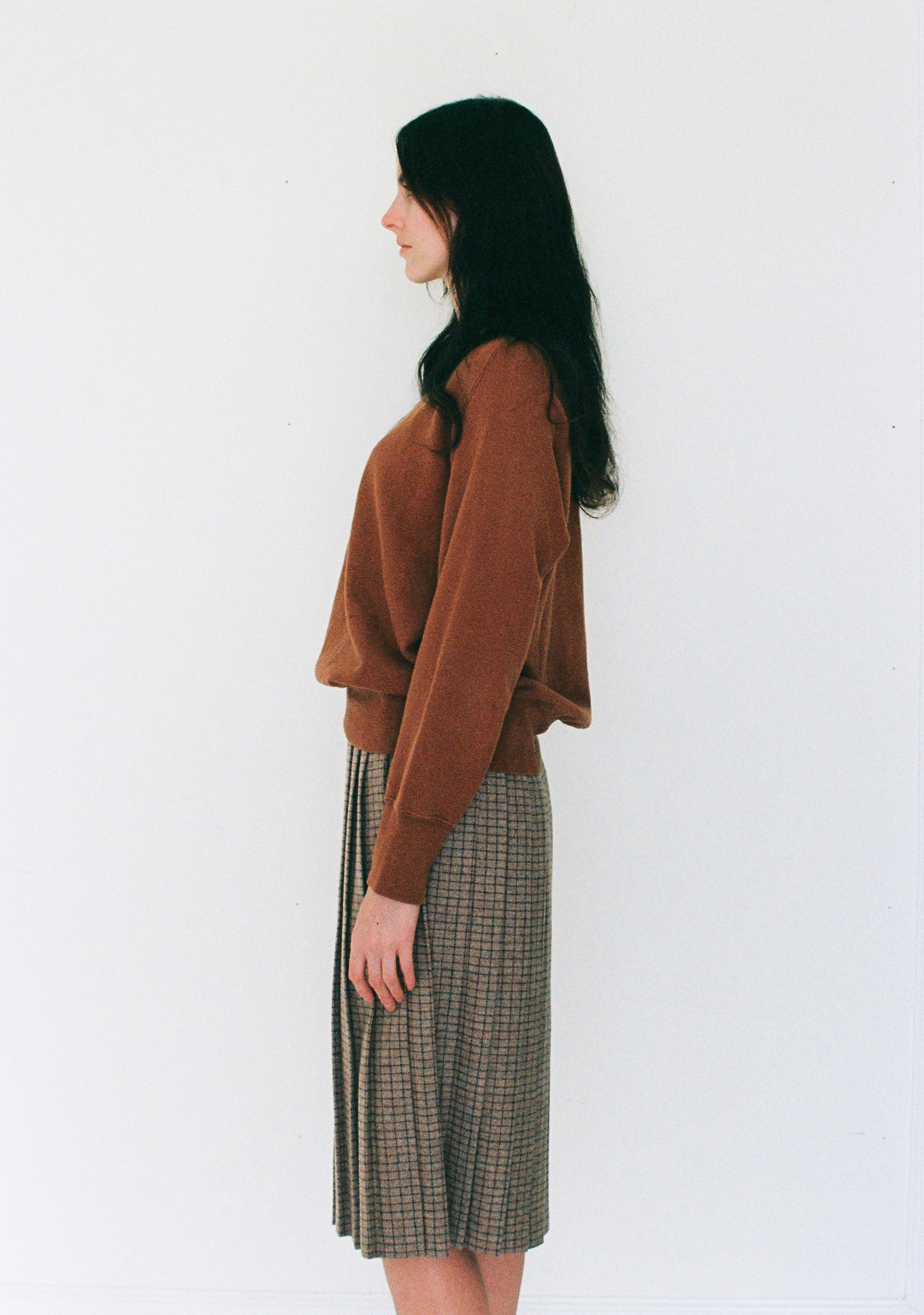 Woman wearing a brown sweater and plaid skirt against a white background