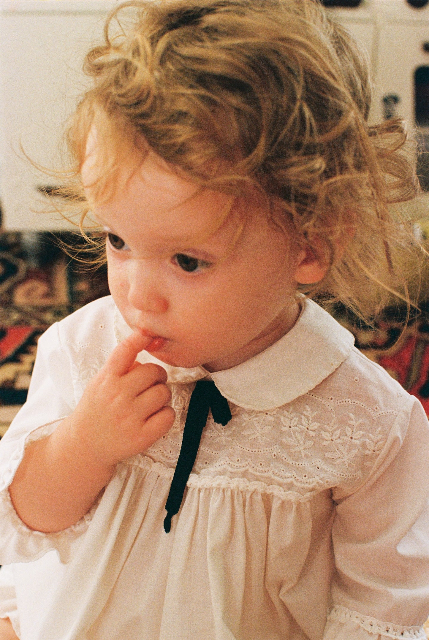 Child wearing a white dress with lace details and a black bow tie.