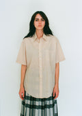 Woman wearing a beige shirt and plaid skirt against a white background