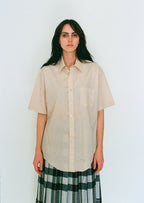Woman wearing a beige shirt and plaid skirt against a white background