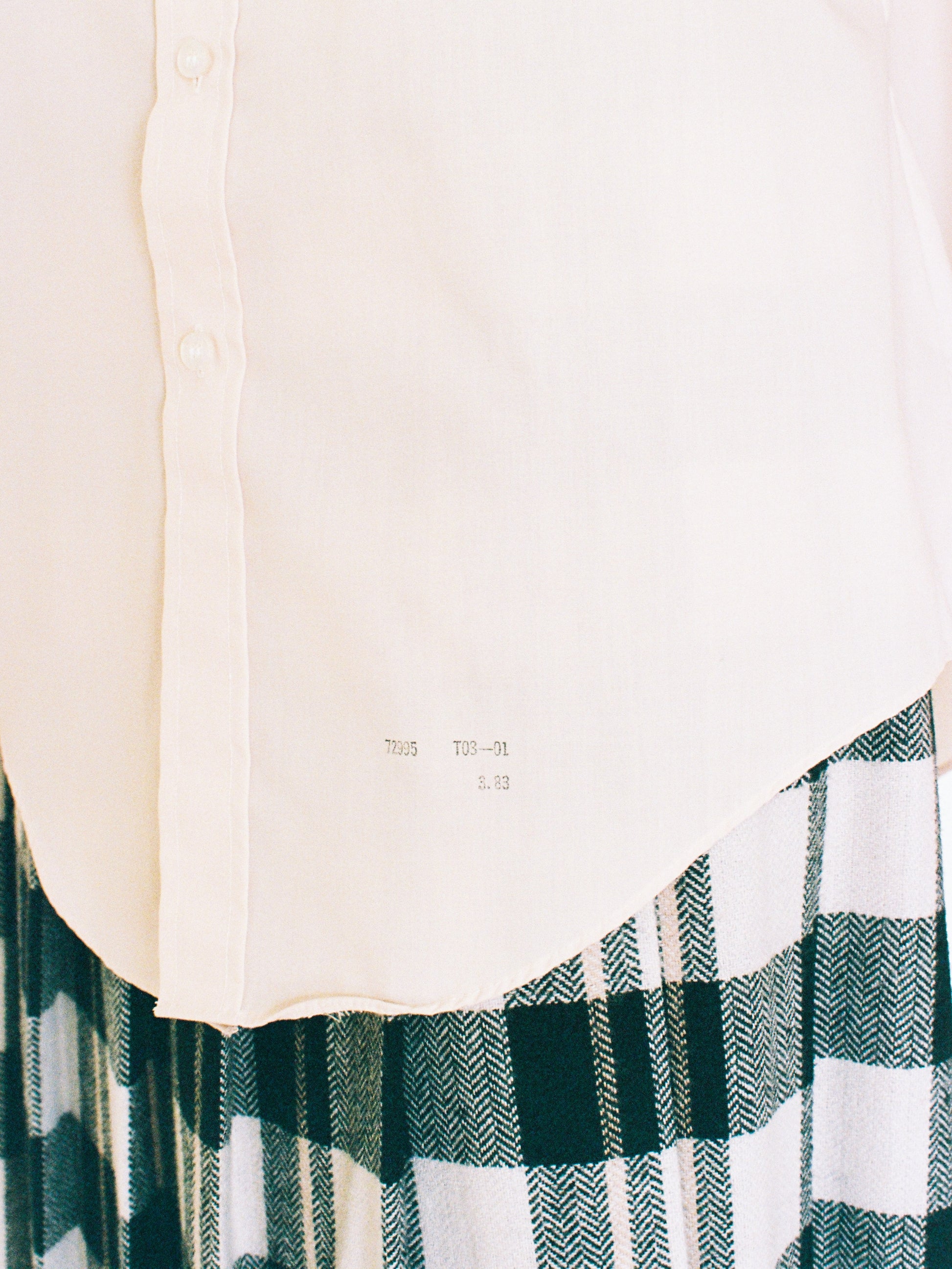 Close-up of a white shirt with a plaid pattern skirt on a plain background