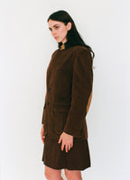 Woman wearing a brown jacket and plaid skirt against a white background