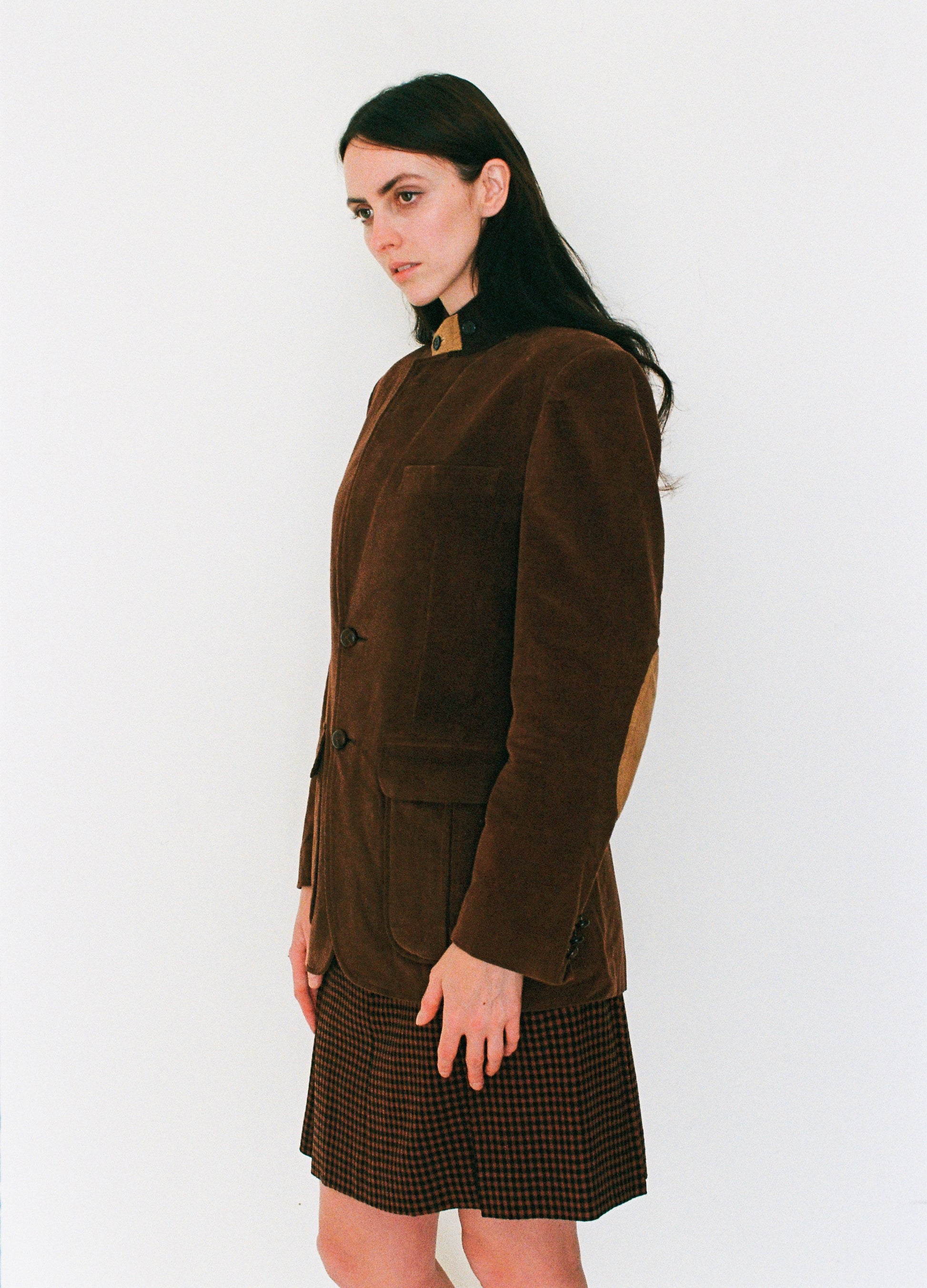 Woman wearing a brown jacket and plaid skirt against a white background