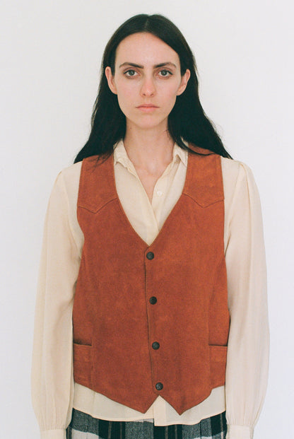 Person wearing a orange leather vest over a white shirt on a plain background
