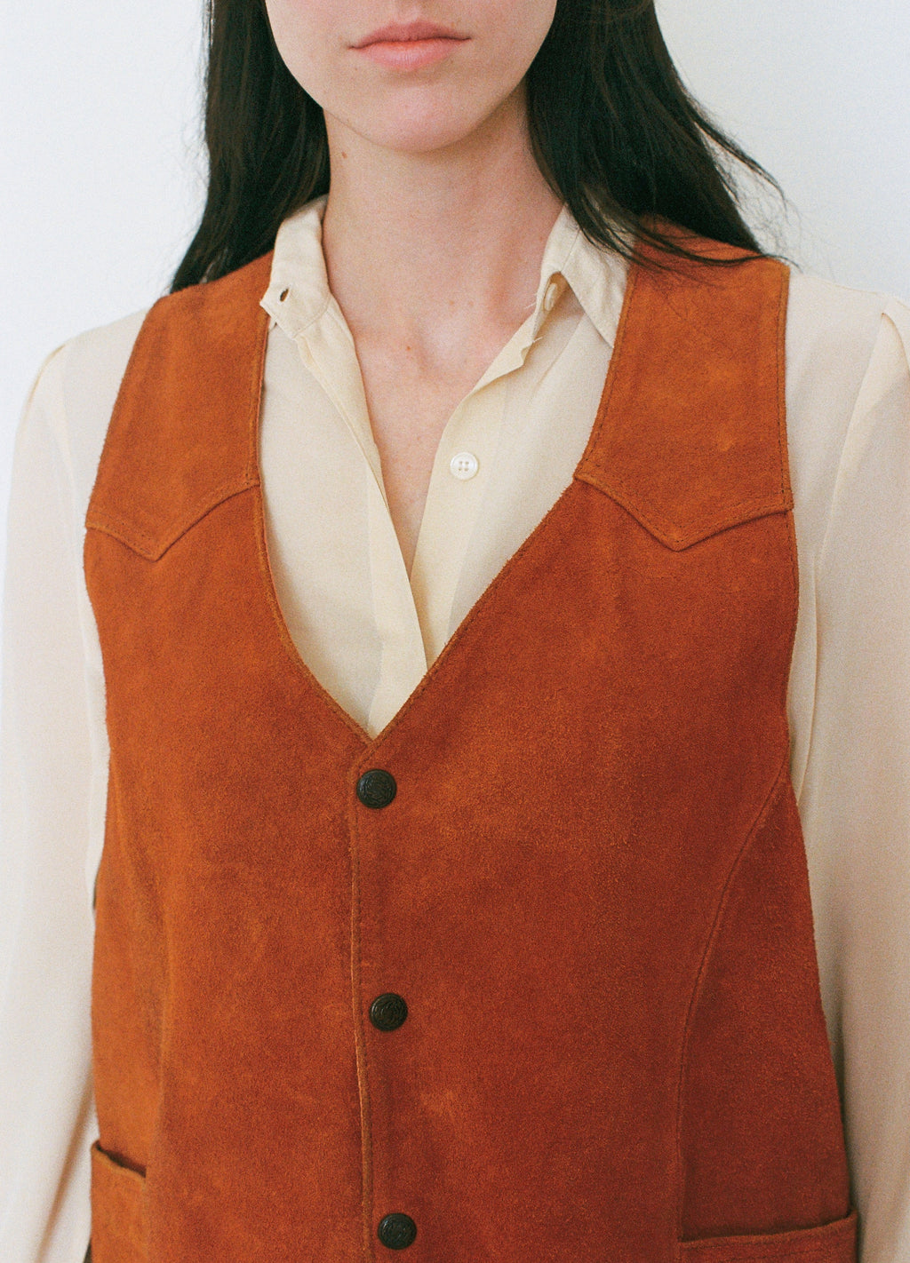 Person wearing a orange leather vest over a white shirt against a plain background