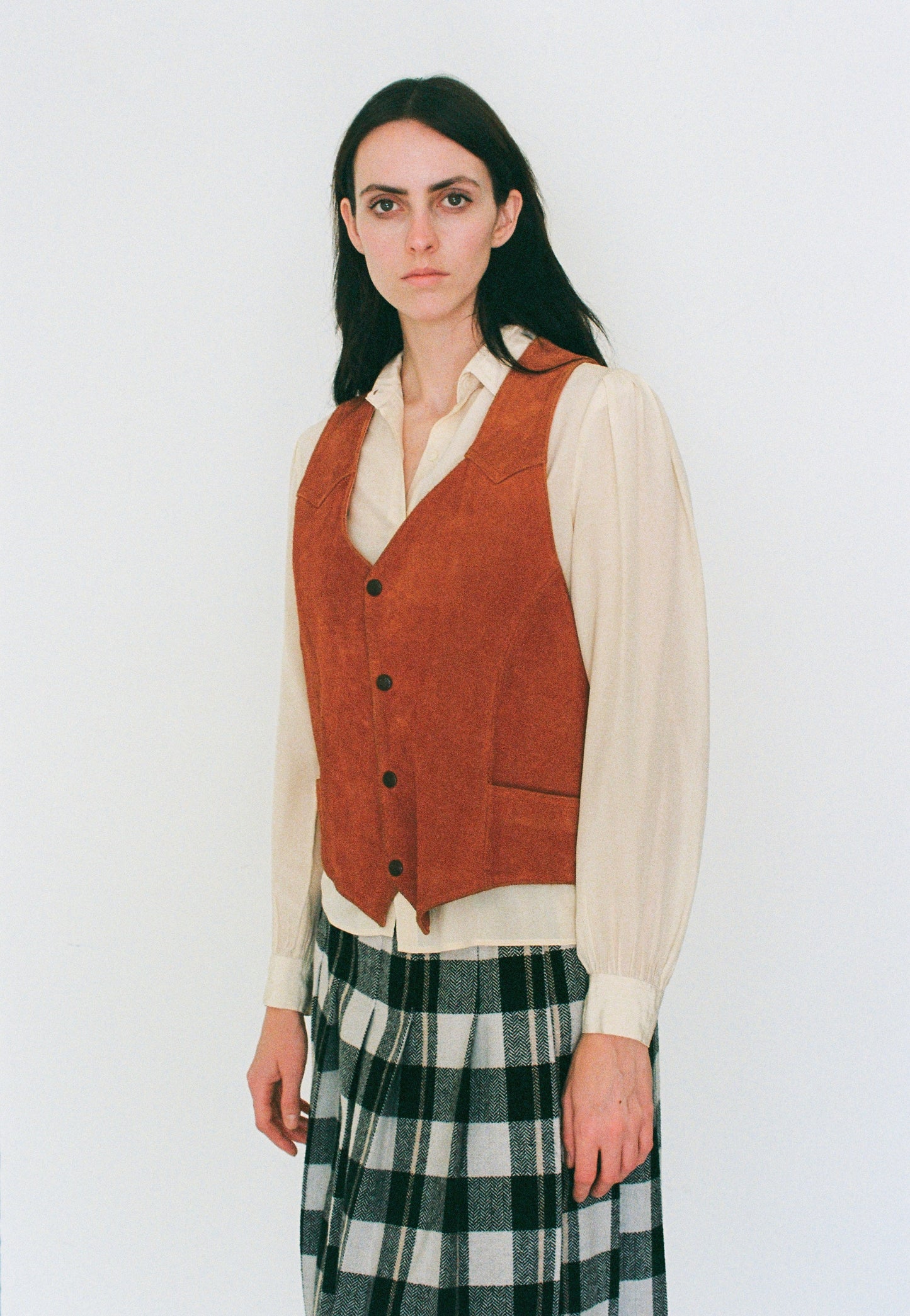 Woman wearing a orange vest over a white shirt with a plaid skirt on a white background