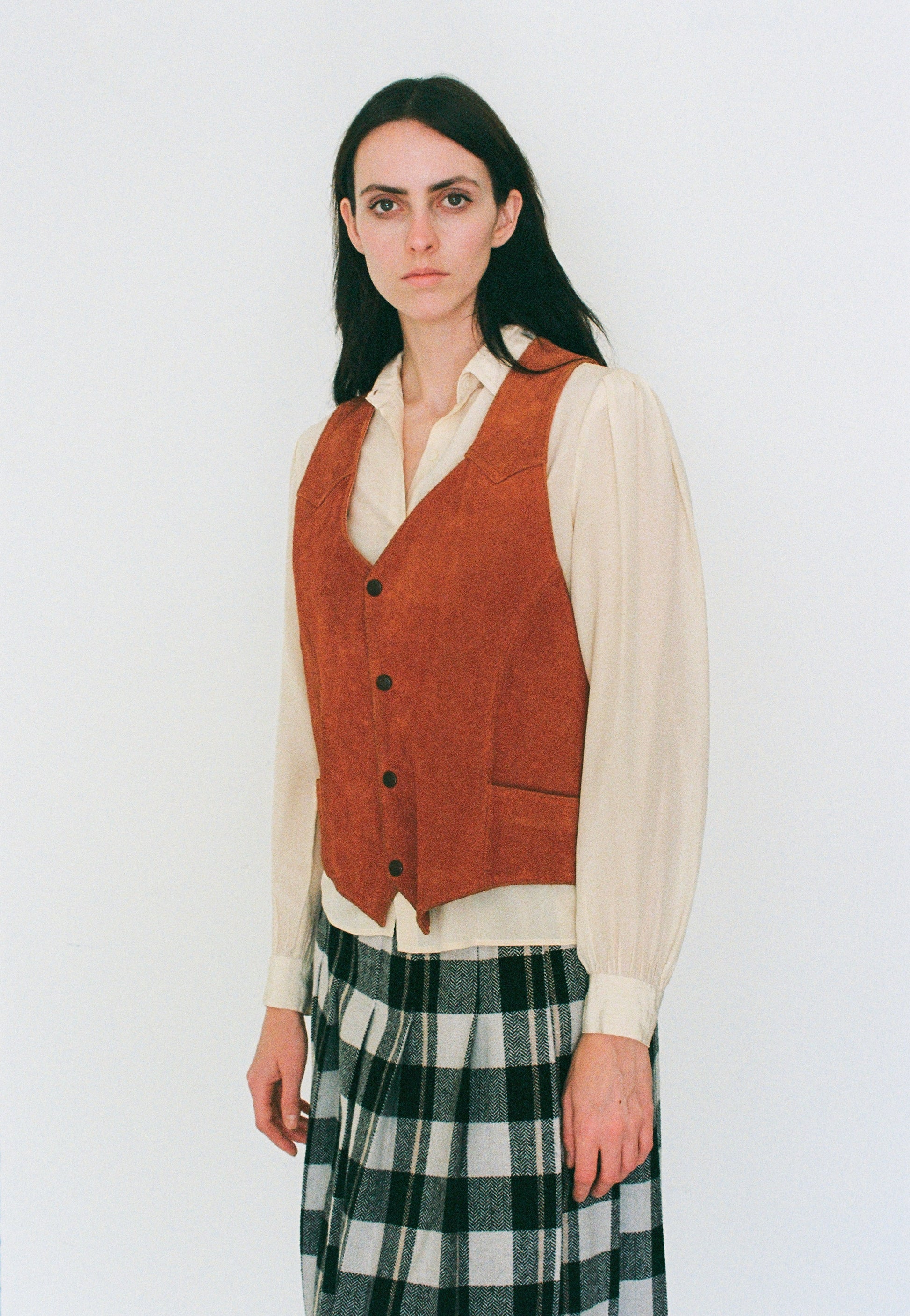 Woman wearing a orange vest over a white shirt with a plaid skirt on a white background