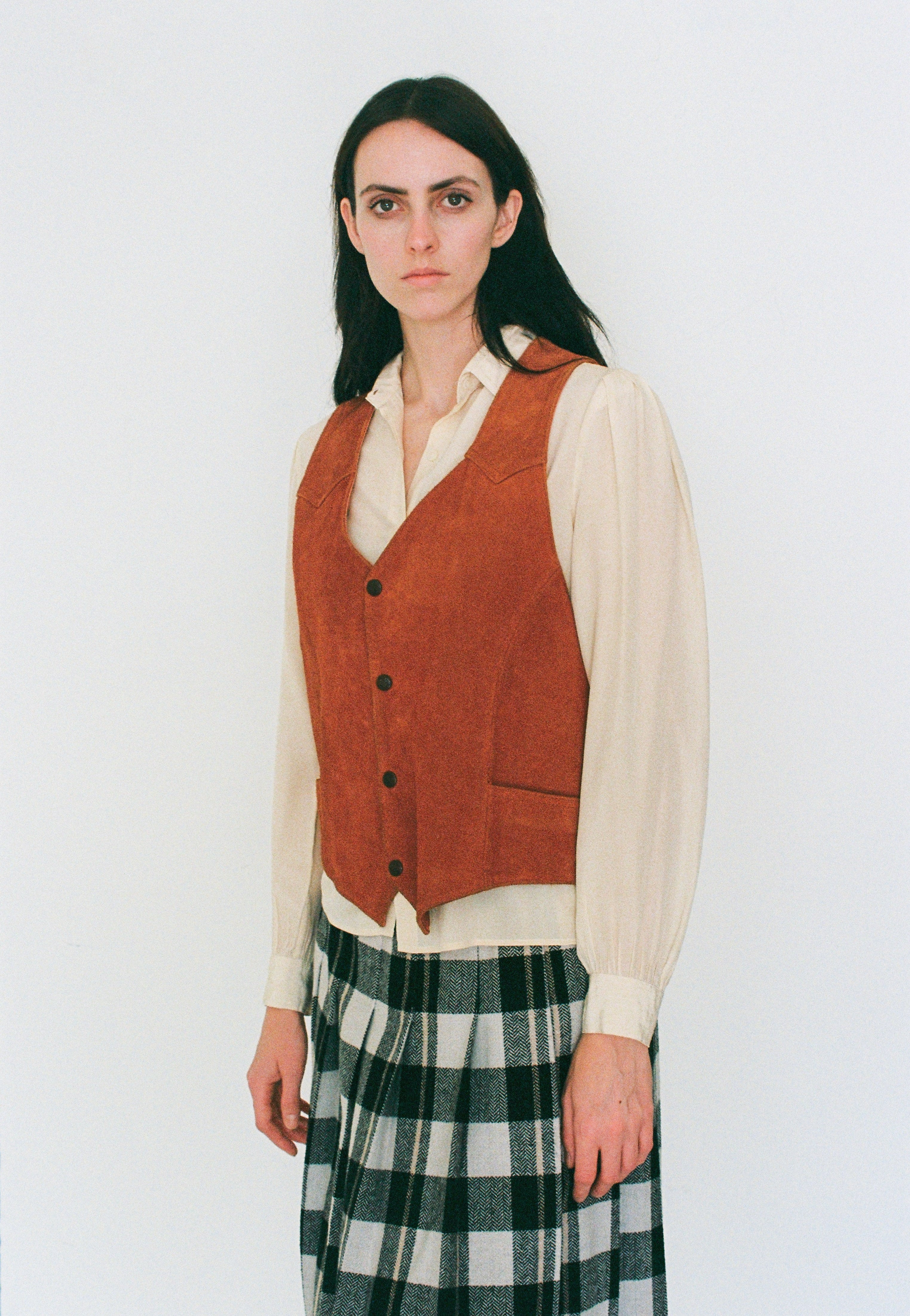 Woman wearing a orange vest over a white shirt with a plaid skirt on a white background