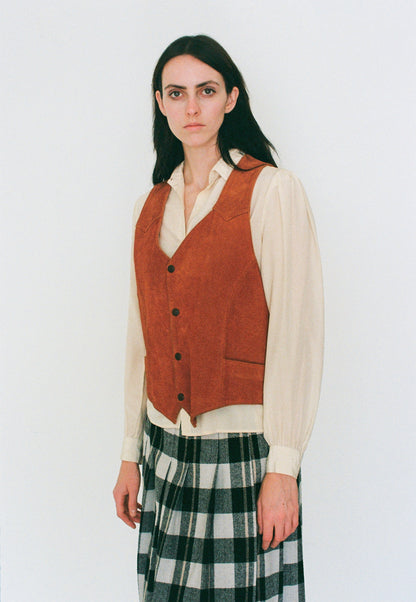 Woman wearing a orange vest over a white shirt with a plaid skirt on a white background