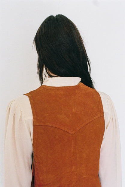 Person wearing a orange suede vest over a white shirt against a plain background