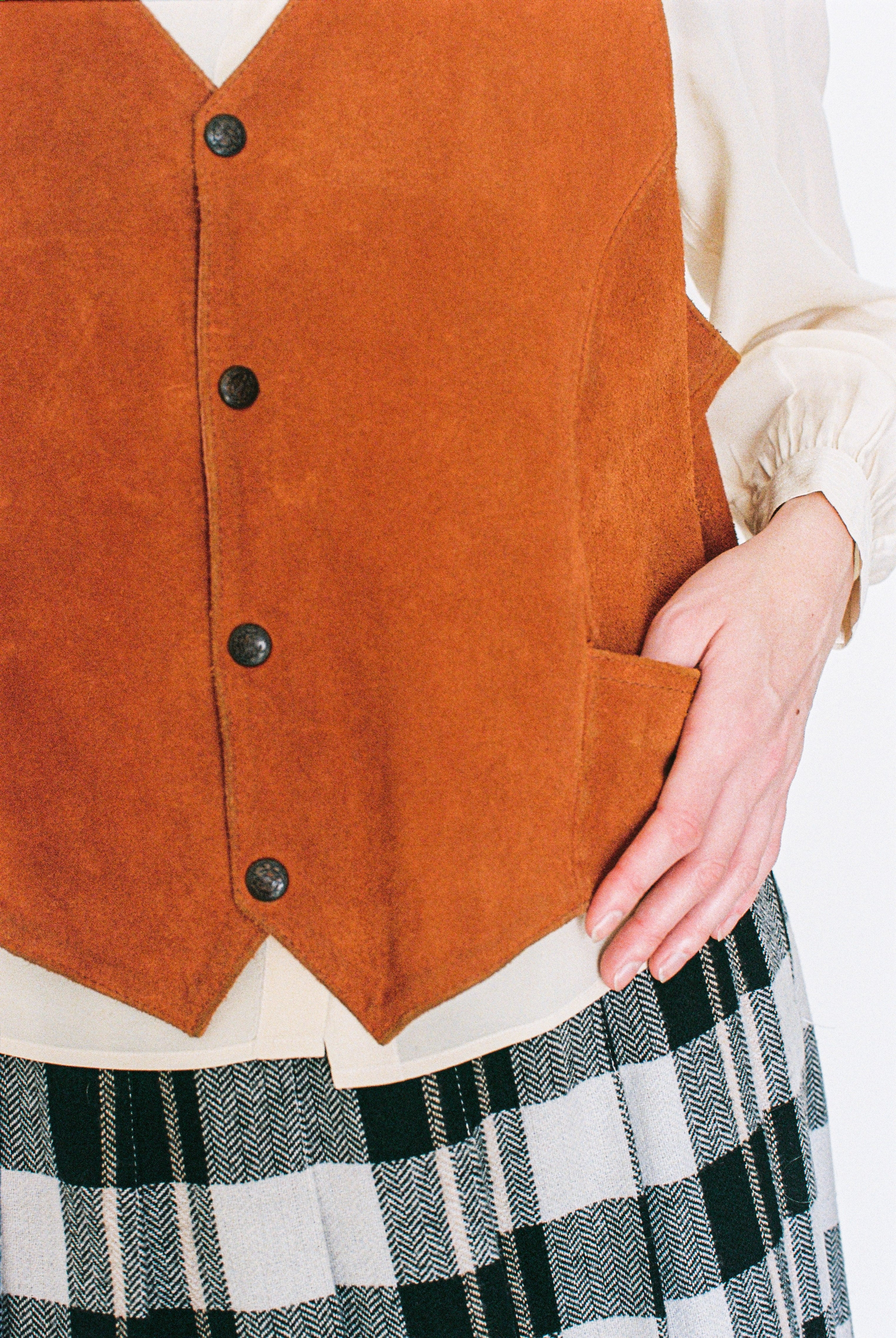 orange button-up vest over a white shirt and plaid skirt on a plain background