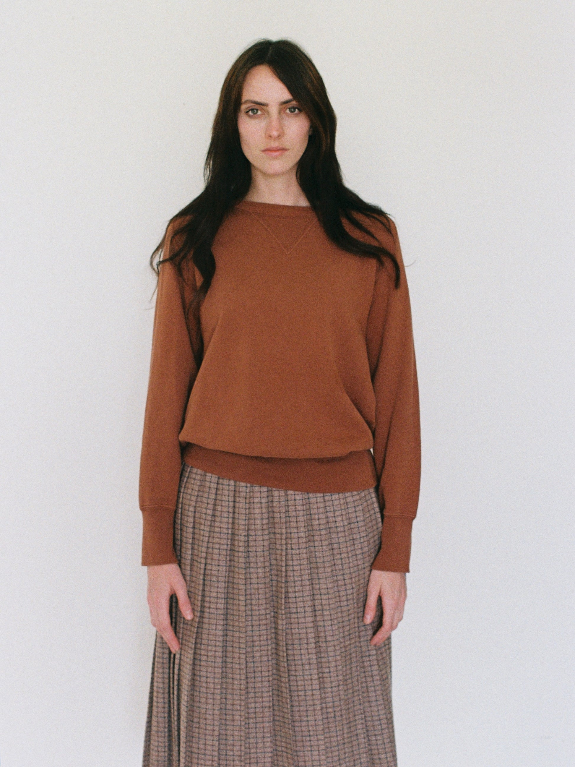 Woman wearing a brown sweater and plaid skirt against a white background
