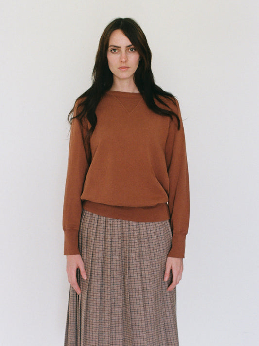Woman wearing a brown sweater and plaid skirt against a white background