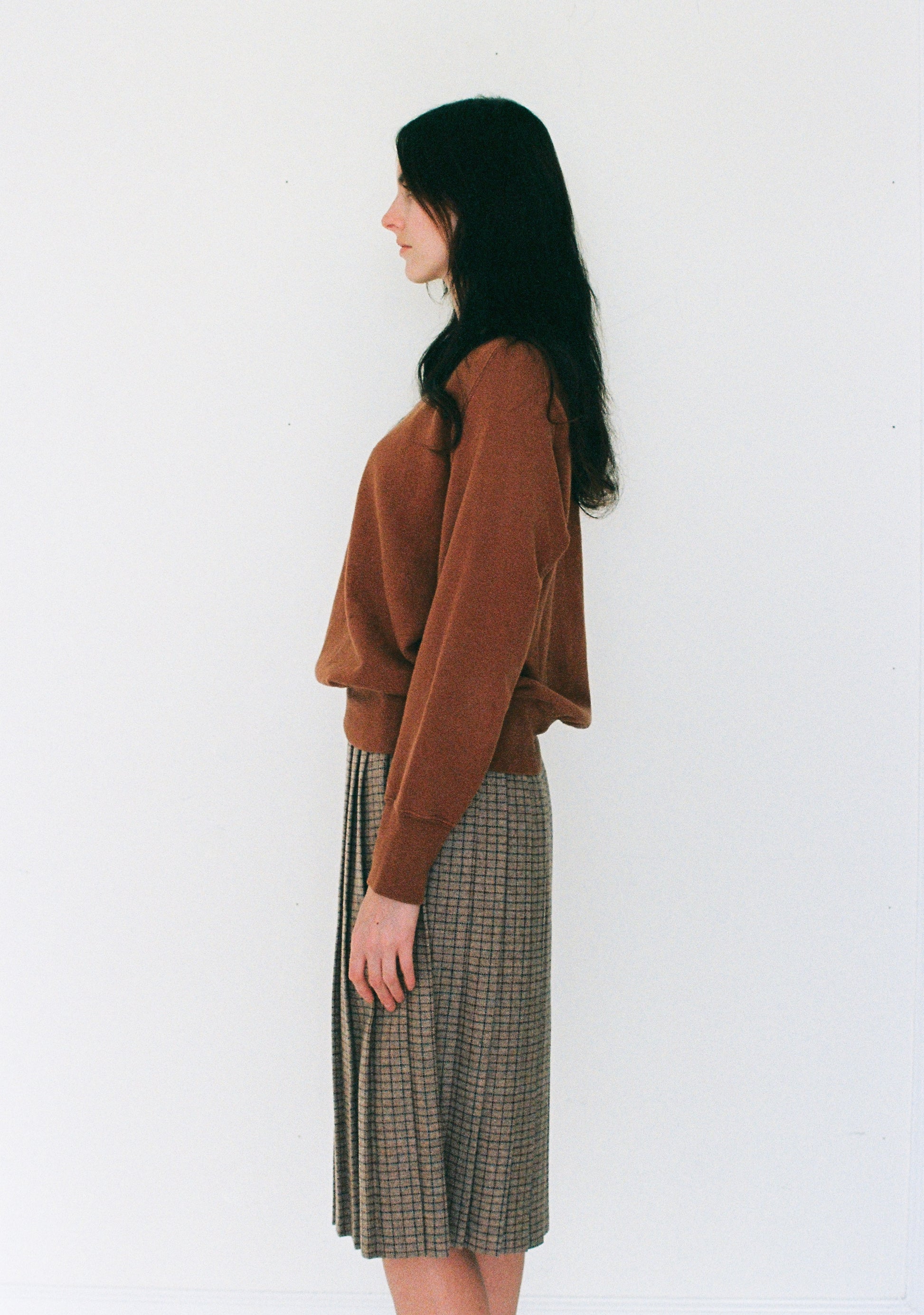 Woman wearing a brown sweater and plaid skirt against a white background