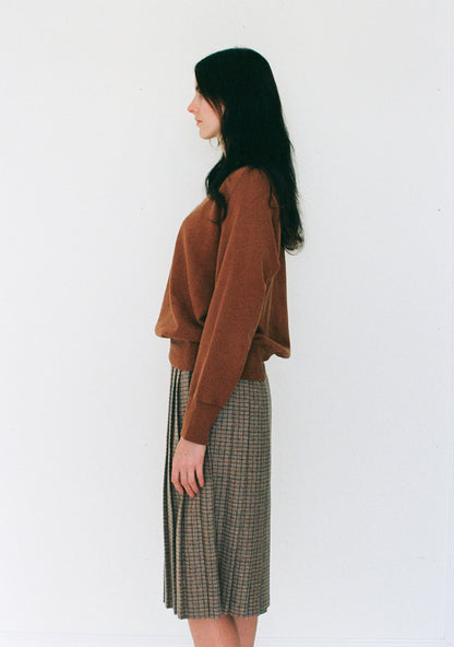 Woman wearing a brown sweater and plaid skirt against a white background