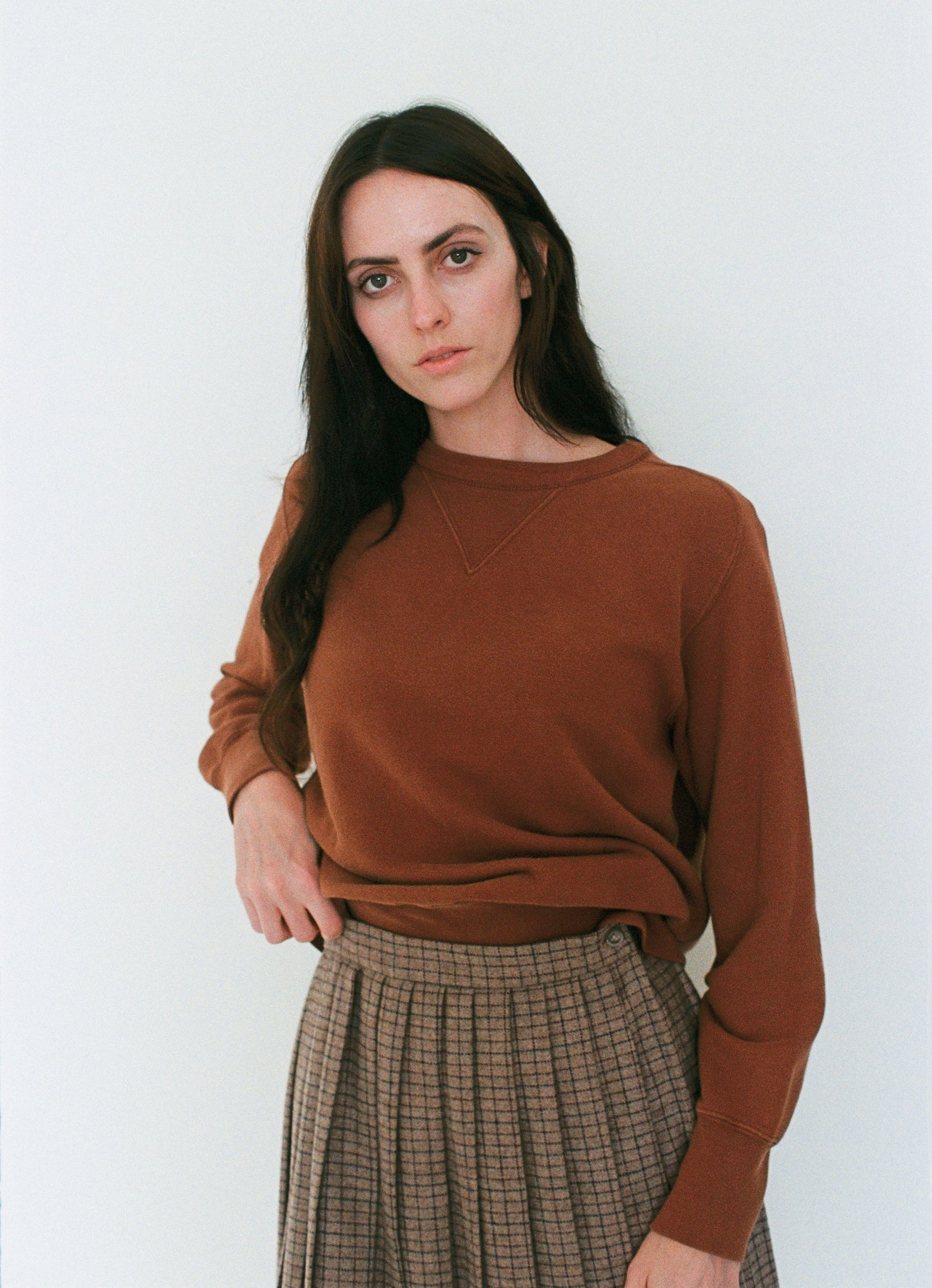 Woman wearing a brown sweater and plaid skirt against a white background