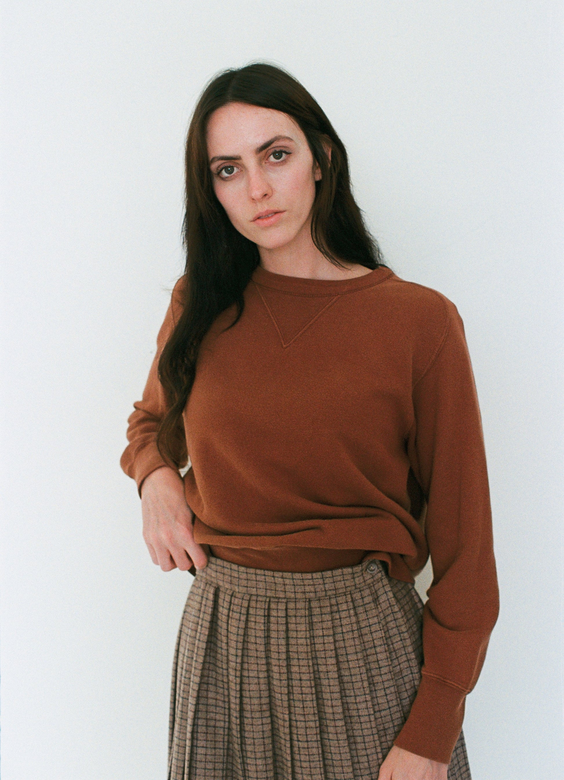 Woman wearing a brown sweater and plaid skirt against a white background