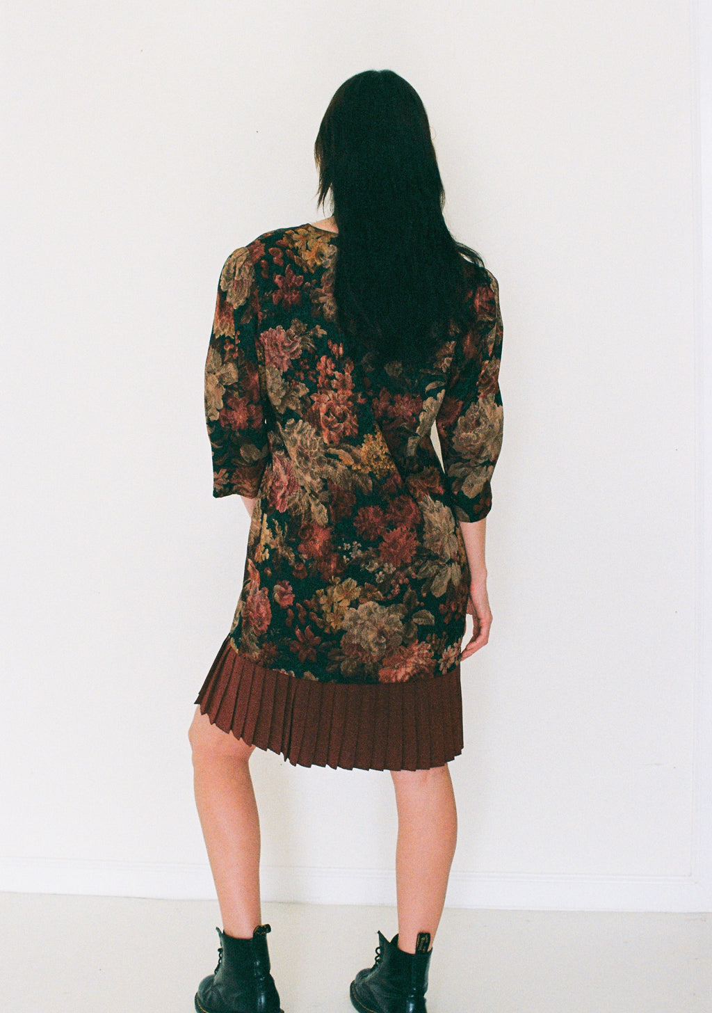 Person wearing a floral dress with pleated skirt against a white background