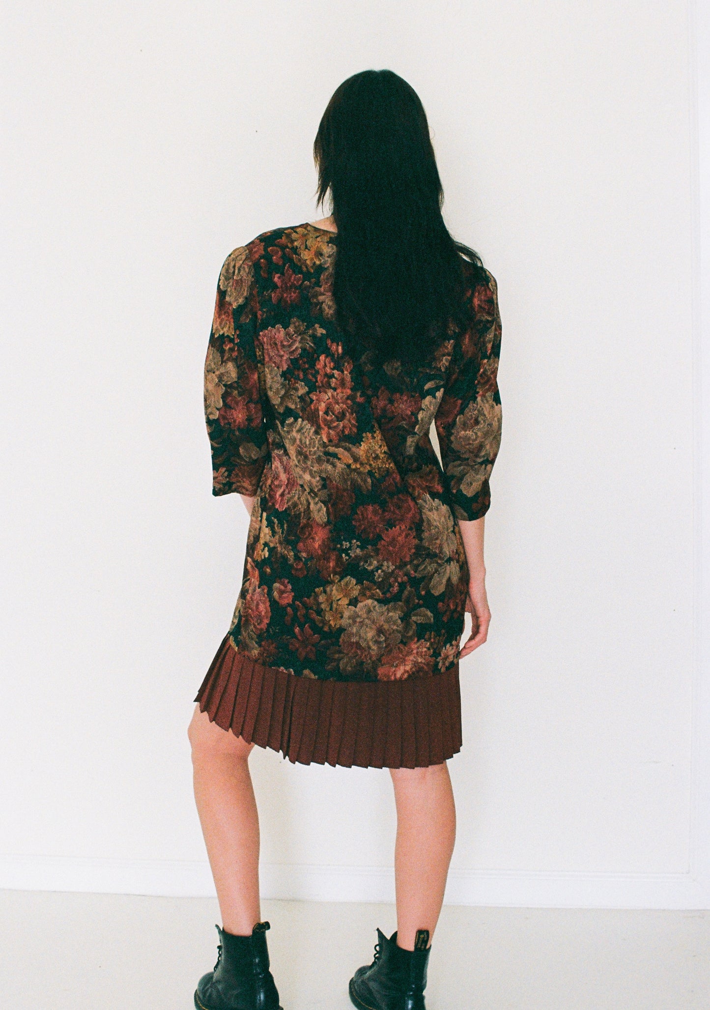 Person wearing a floral dress with pleated skirt against a white background