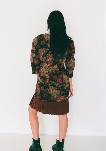 Person wearing a floral dress with pleated skirt against a white background