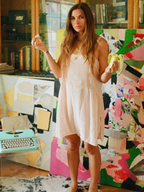 Woman in a light dress holding a banana in front of a colorful abstract painting.