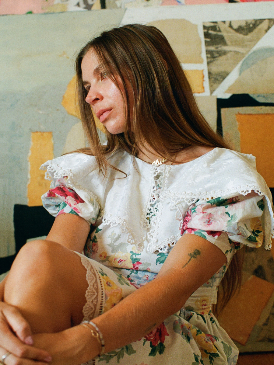 Woman in a floral dress sitting against a colorful abstract wall.