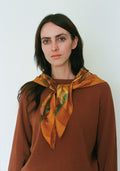Woman wearing a brown top and patterned orange scarf against a white background