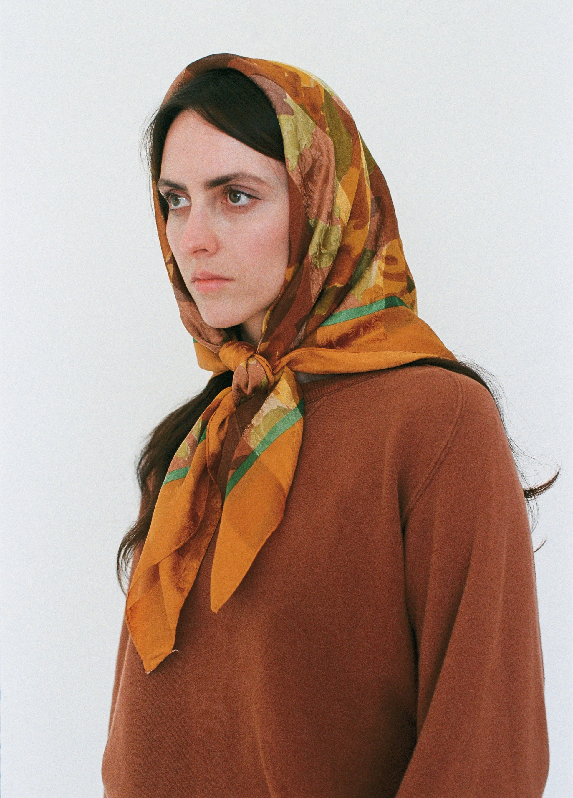 Woman wearing a patterned headscarf and brown outfit against a white background