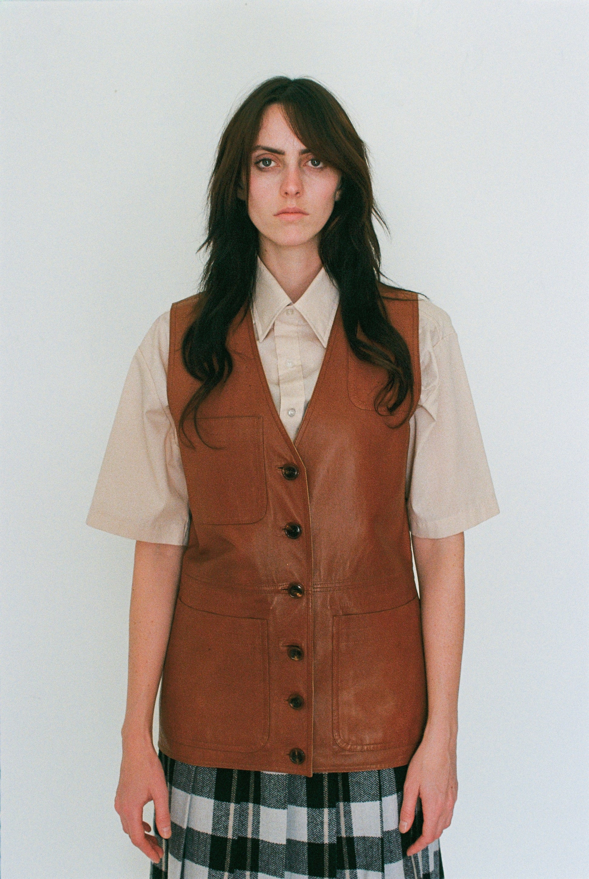 Person wearing a brown leather vest over a beige shirt with a white background