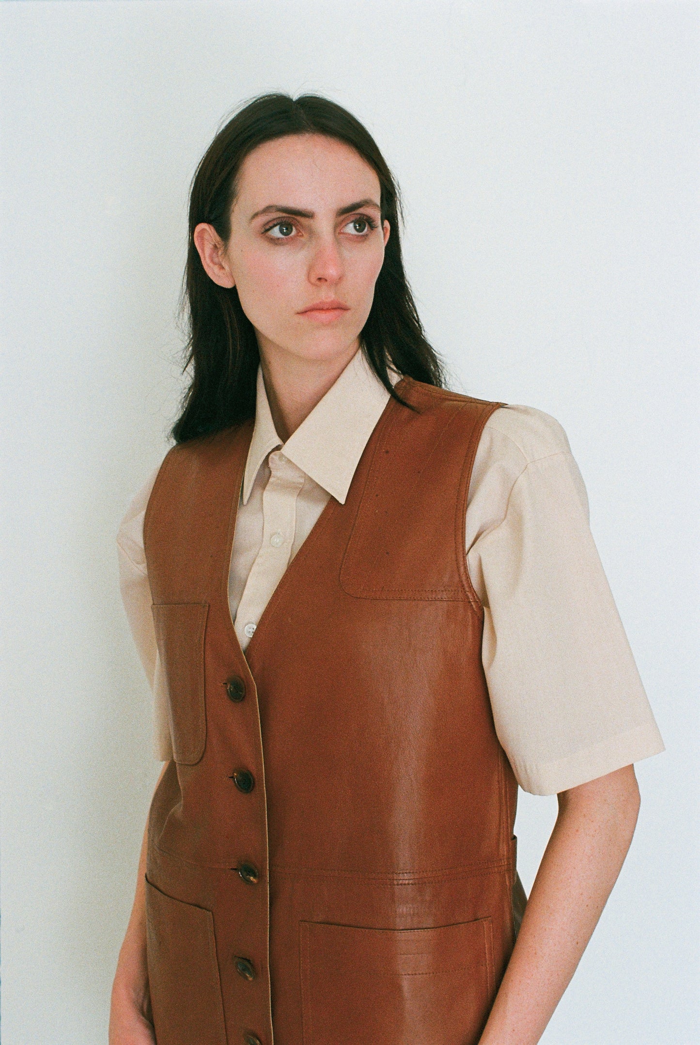 Woman wearing a brown leather vest over a beige shirt against a white background