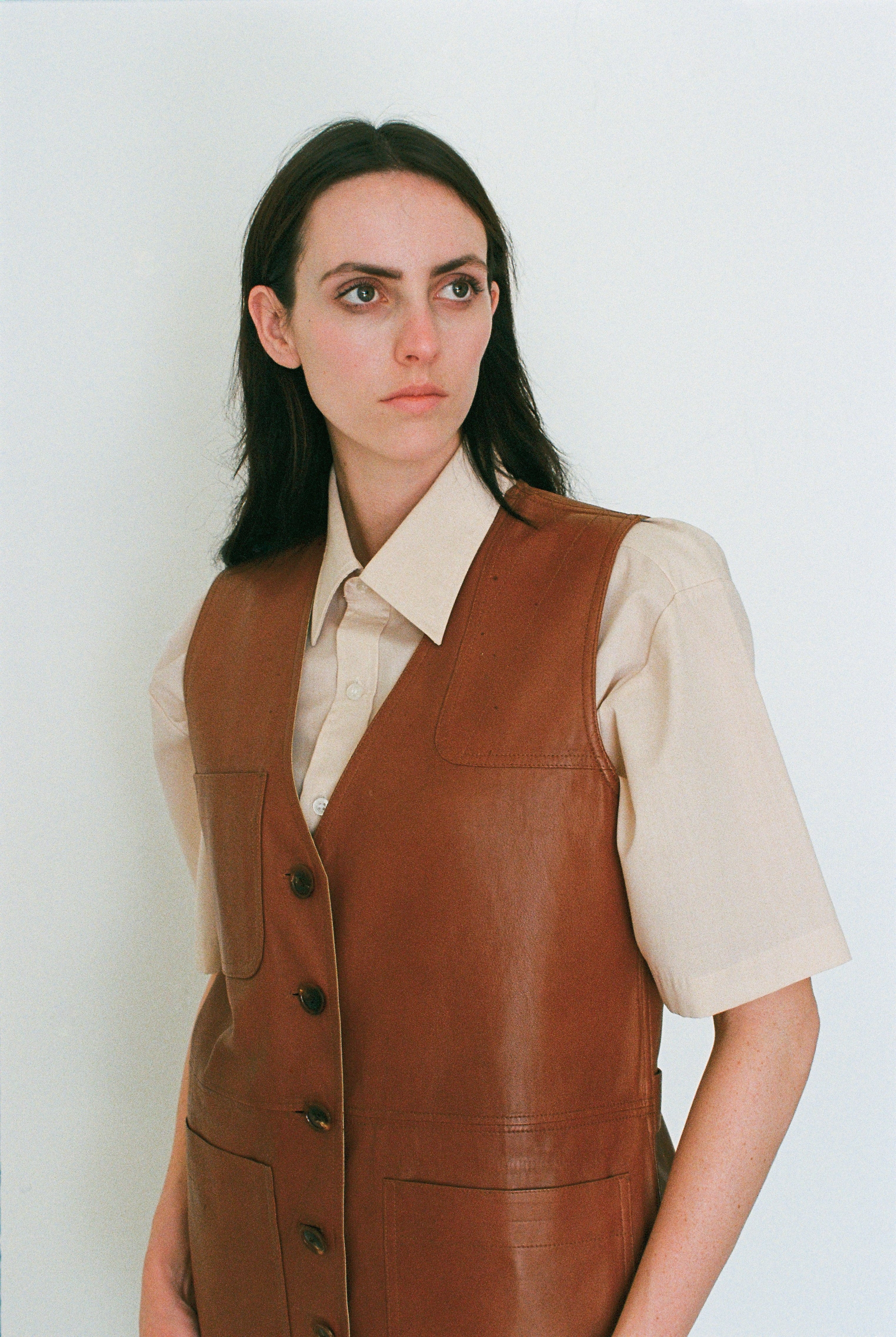 Woman wearing a brown leather vest over a beige shirt against a white background