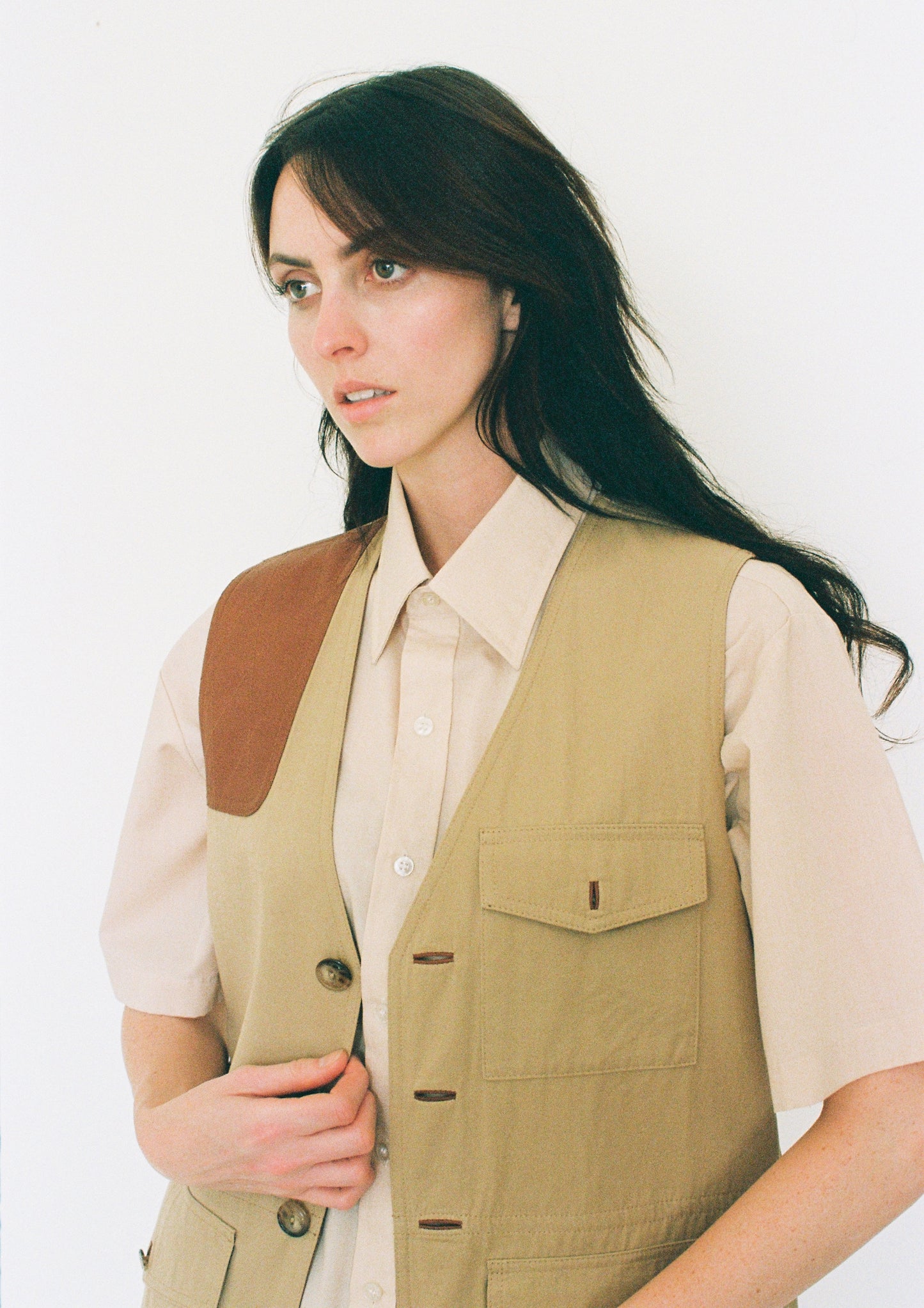 Woman wearing a beige shirt and khaki vest against a white background
